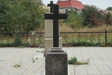 black marble cross on the monument at the grave in the cemetery against a blue sky and green tree branches