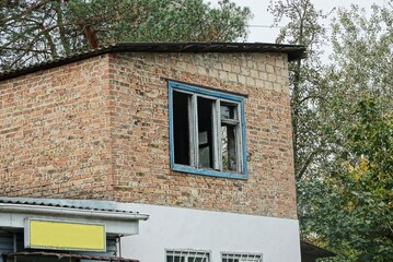 brown bricks attic of an old house with a broken window on the street against a background of sky and green vegetation