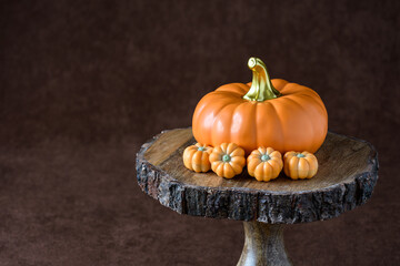 Fall harvest, orange ceramic pumpkin surrounded by chocolate shaped as pumpkins, on a wooden cake stand, against a brown background
