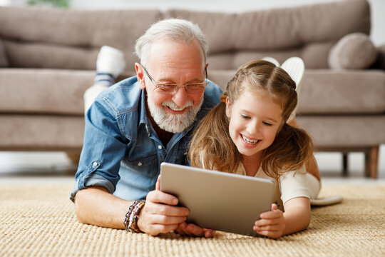 Grandfather and granddaughter using tablet on floor.
