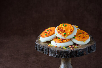 Fall harvest, orange frosted sugar cookies with colorful sprinkles, on a wooden cake stand, against a brown background
