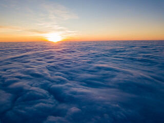 Fototapeta premium Sunset over curly clouds, aerial high flight. The last rays of the sun shine on the clouds.