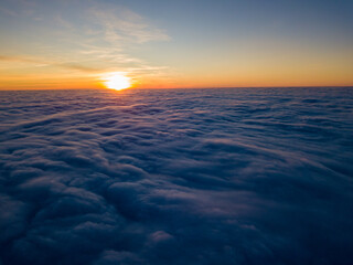 Sunset over curly clouds, aerial high flight. The last rays of the sun shine on the clouds.