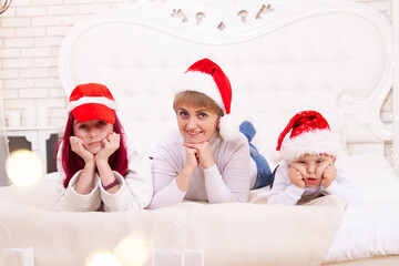 Boy with Down syndrome, his sister and mother in Santa hats lie on the couch, disabled children,...