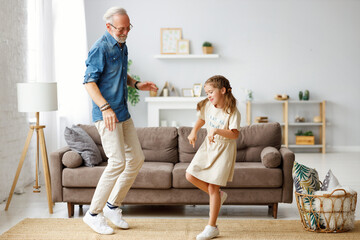 Grandfather dancing with granddaughter at home.
