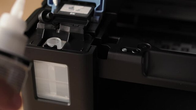 Video instruction, technology, media, office, stationery concept - close-up of male hands preparing new inkjet printer for launch. step 10: insert nozzle of bottle into inlet stand upside down pur ink