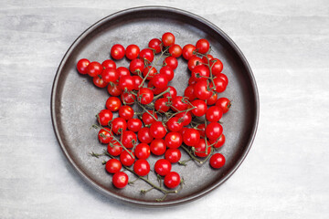 Top view of a black ceramic bowl with juicy organic sweet small tomatoes on the vine
