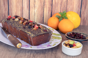 Homemade lemon and orange pudding with fruits on a white platter with vintage-style flower drawings on a wooden table, some citrus fruits, knife and a rustic machimbre background