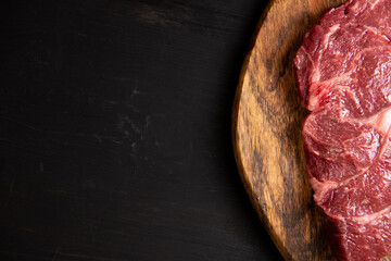 a fresh piece of juicy marbled beef black angus lies on a cutting board on a black wooden table. with free space for text design or restaurant menu logo. Horizontal photo. Food background.