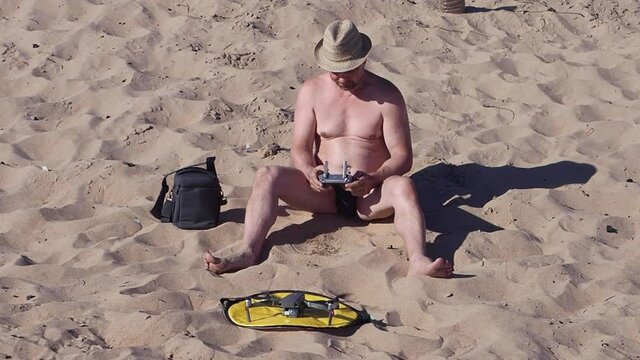 A man sitting on a sandy beach with a remote control controls an airplane. Slow motion