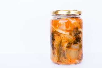 Jar of Kimchi, typical Korean food made with Korean cabbage and spices on black, white background.
