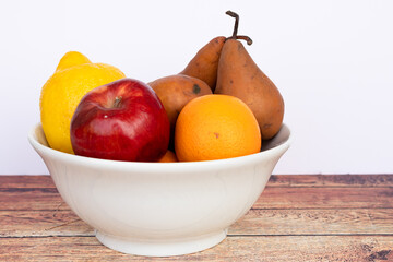Pears of the Kaiser Alexander variety , apple, orange and other fruits in a white bowl on a wooden table and white background