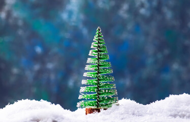 Little Christmas tree toys in snowdrift, winter New Year concept. Festive composition on blue background with lights and snowflakes