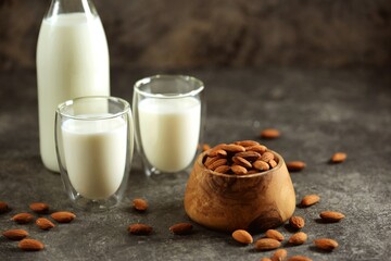 Almond milk in glass with almonds nuts on grey concrete background. Vegan food.