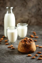 Almond milk in glass with almonds nuts on grey concrete background. Vegan food.