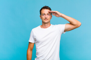 young handsome man greeting the camera with a military salute in an act of honor and patriotism,...