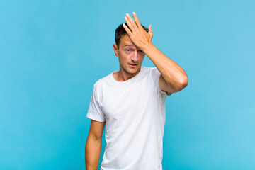 young handsome man raising palm to forehead thinking oops, after making a stupid mistake or...