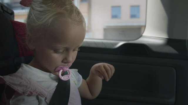 A portrait of a little girl, travelling by car with a pacifier in her mouth