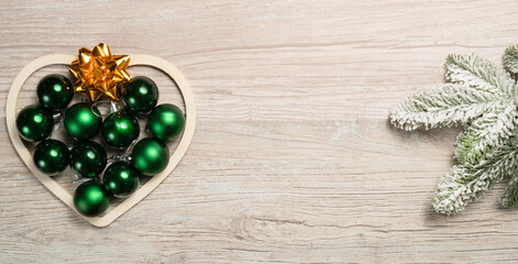 Christmas heart arranged with green baubles and golden bows on wooden background