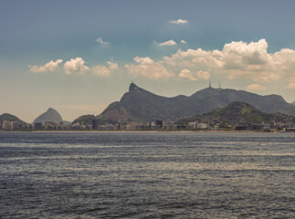 Niteroi, Brazil - December 24, 2008: Christ the Redeemer statue on hill and Rio de Janeiro cityscape  seen from Gragoata coastal neighborhood across the Guanabara bay. Light blue late afternoon clouds