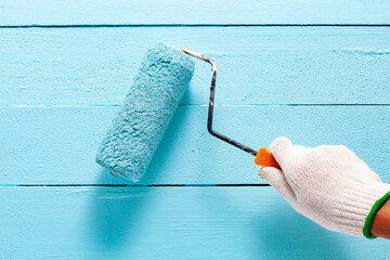 Man's hand holding roller brush paint blue color on blue wooden color wall background.