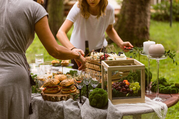 Anonymous female caterers setting up a table for a garden party with fresh organic, farm-to-table tapas