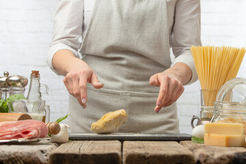 Close-up view of chef in uniform kneads the dough by hands on black chopped board for cooking pasta alla carbonara. Backstage of preparing traditional italian dish on white background. Frozen motion