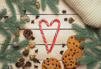 Christmas background with a knitted jacket with spruce branches, Christmas toys, cookies, heart-shaped candies in the center, with a nice warm soft light. Christmas background on wooden white boards