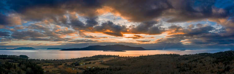 Panoramic Aerial Sunset View of an Island In the Pacific Northwest. Dramatic clouds highlight this drone shot of surrounding islands in the Salish Sea area of western Washington state. Lummi Island.