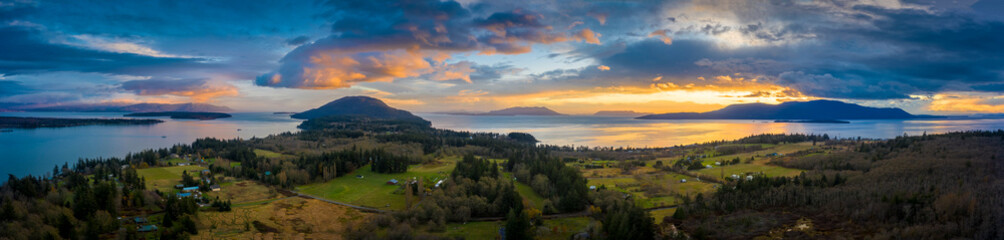 Panoramic Aerial Sunset View of an Island In the Pacific Northwest. Dramatic clouds highlight this drone shot of surrounding islands in the Salish Sea area of western Washington state. Lummi Island.