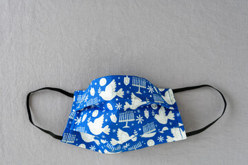 Handmade fabric mask on a silver background, celebrate Hanukkah with Jewish symbols on a blue mask
