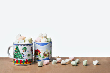 Obraz na płótnie Canvas dos tazas de navidad con chocolate y bombones de colores, en mesa decorada con mas bombones con fondo blanco