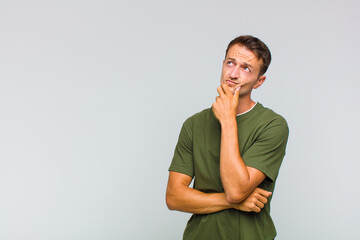 young handsome man thinking, feeling doubtful and confused, with different options, wondering which...