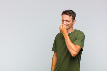 young handsome man feeling disgusted, holding nose to avoid smelling a foul and unpleasant stench