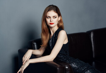 Elegant woman in a dark dress on a leather sofa and evening makeup