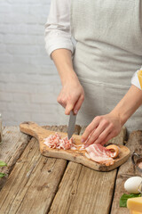 Close-up view of professional chef in white uniform cuts with knife bacon on wooden chopped board for cooking pasta alla carbonara. Backstage of preparing traditional italian dish.