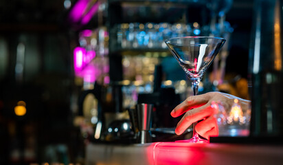 Bartender preparing tasty mixed tasty alcoholic drink in empty martini cocktail glass on bar counter for customer in nightclub. Celebration party, nightlife business and alcohol addiction concept
