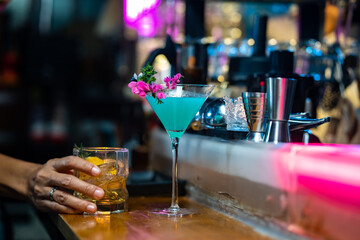 Bartender preparing tasty mixed blue alcoholic drink in decorated cocktail glass on bar counter for customer in nightclub. Celebration party, nightlife business and alcohol addiction concept