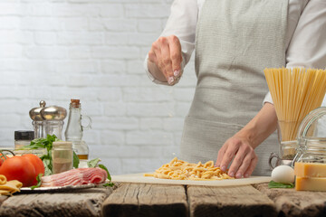 Professional chef in white uniform salts handmade spaghetti for cooking pasta alla carbonara. Backstage of preparing traditional italian dish on white background. Frozen motion. Recipe book.