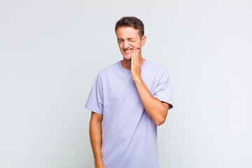young handsome man holding cheek and suffering painful toothache, feeling ill, miserable and...