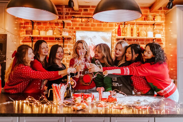 a group of young beautiful women in Christmas sweaters clink glasses