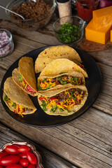 Top view of plate with tasty mexican tacos on rustic wooden table with variety ingredients background. Concept of traditional food.