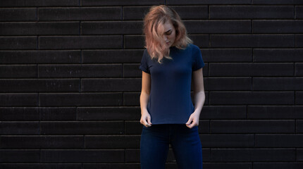 Young blonde woman in blue t-shirt on the background brick wall