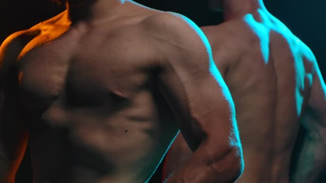 Two athletic naked chested men show off muscles and a strong muscled body. Picture taken in the studio on a black background. Male torso close up. Slow motion.