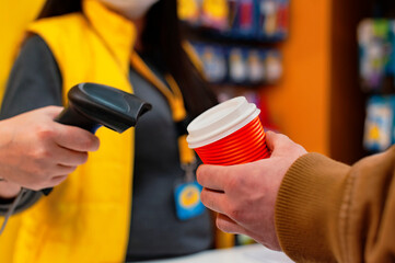 girl seller holds a barcode scanner in her hands and is counting on a man with a glass of coffee in his hand.