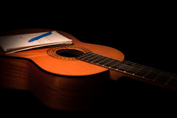 Acoustic guitar and note pad close up on black background. A studio shot with warm lighting,...