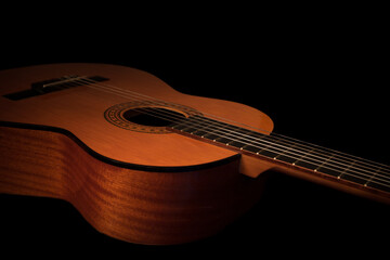 Acoustic guitar isolated on black background, close up. Warmly lit studio shot, ideal for music training, lessons and guitar courses.