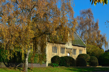 An old English house next to a birch tree in autumn.