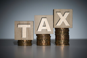 Tax wording on a wooden cube with an ascending stacked coins