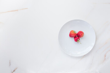  Three strawberries on a large white dish with copy space. The concept of spring and berries from your vegetable garden